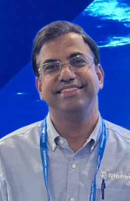 Akhilesh Tripathi, a brown skinned man smiling in front of a watery blue background. 