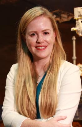 Laurie Barge, a white woman with long blonde hair, is smiling in front of a white scientific instrument.