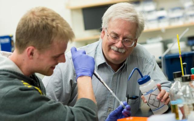 Professor with water wash bottle looks on as a student learns how to use a micropipette