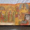 A manuscript open on a table to show two pages of richly colored religious imagery