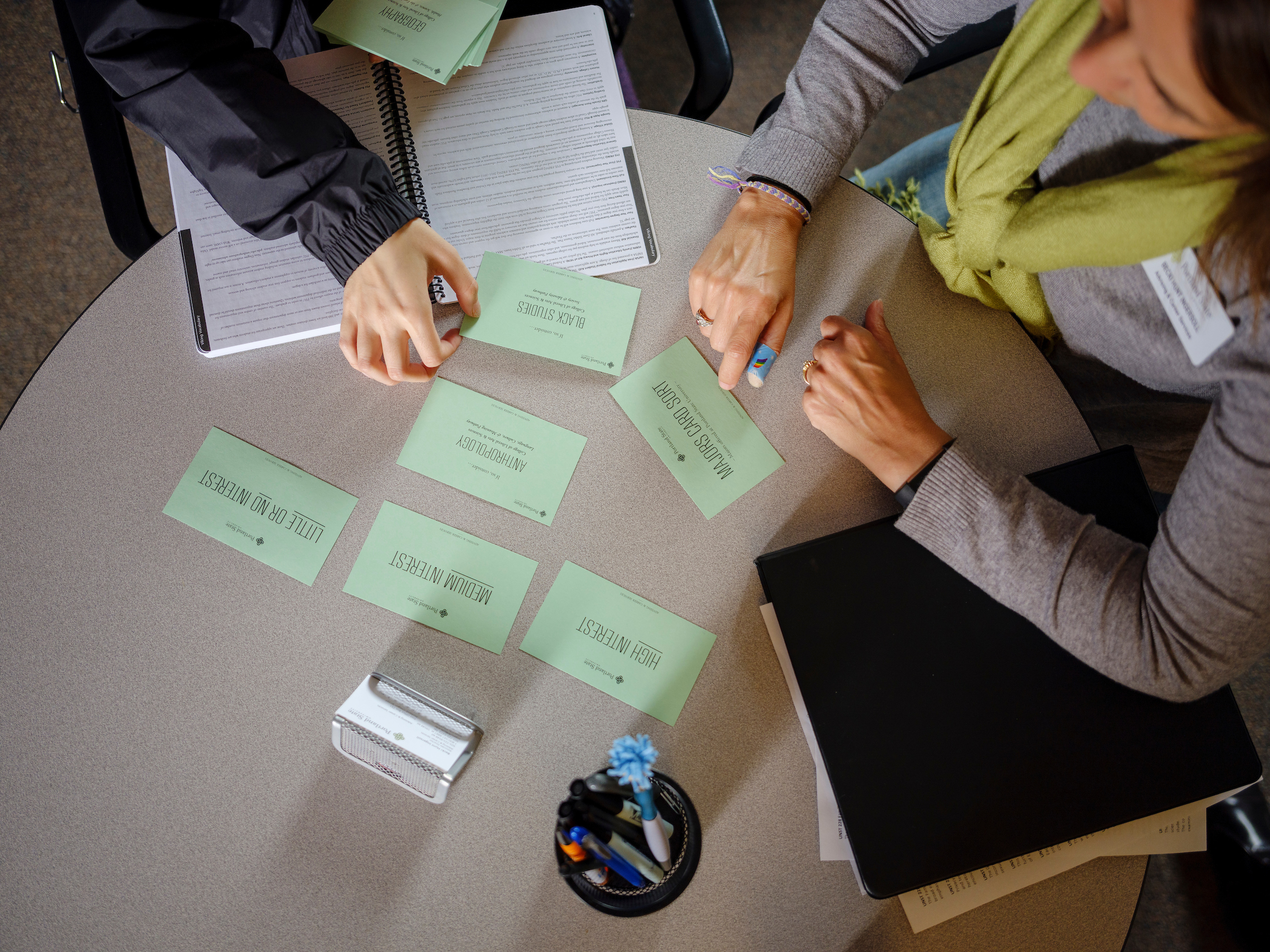 Bird's eye view of advisor and student meeting, pointing to index cards on table