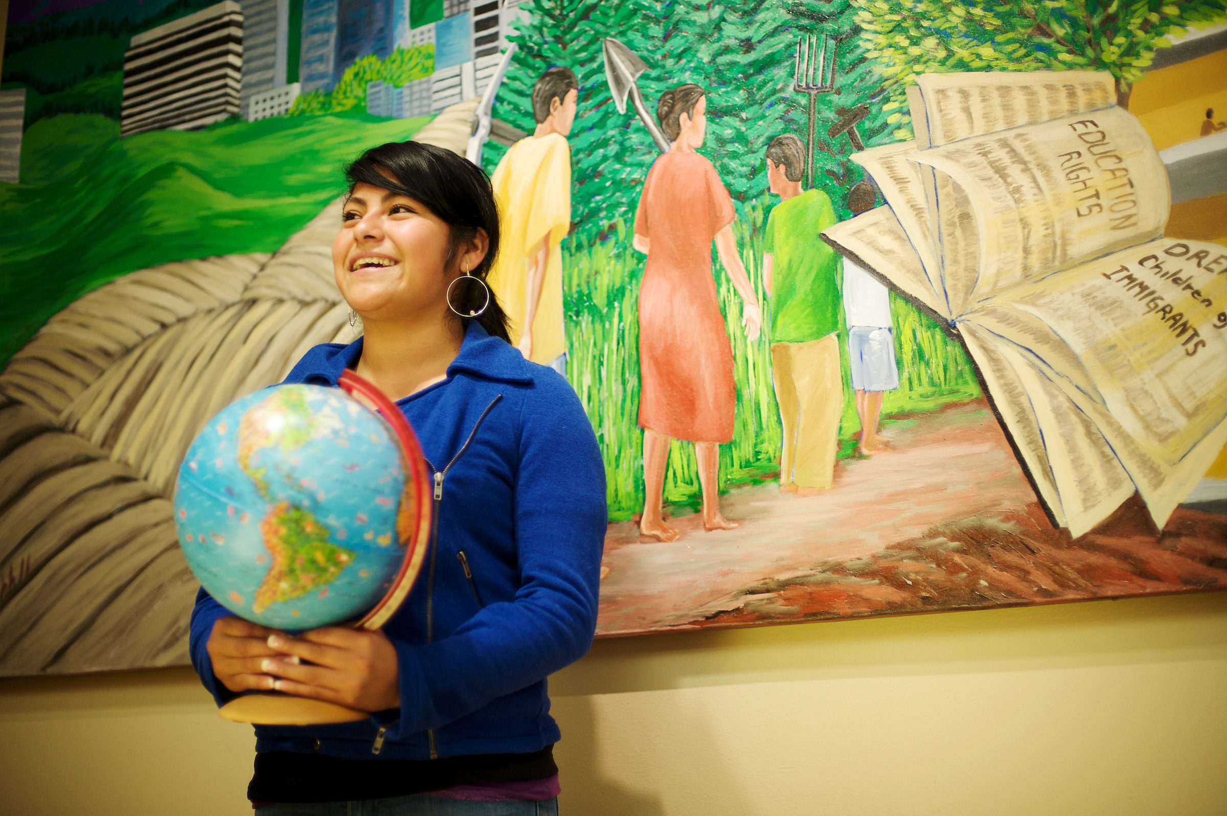 Student holding a globe in front of mural