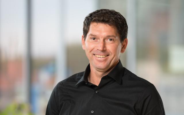 a headshot of Peter Dusicka, wearing a black shirt and smiling at the camera