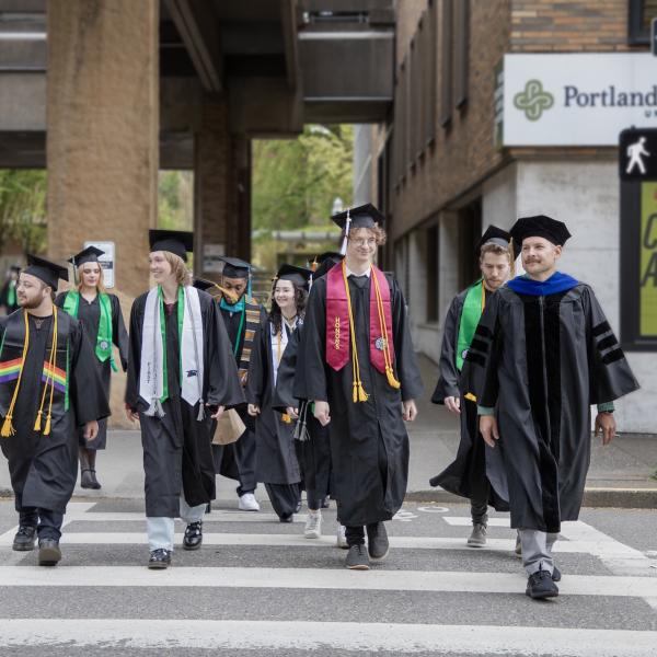 PSU graduates in caps and gowns cross a downtown Portland street near campus before commencement