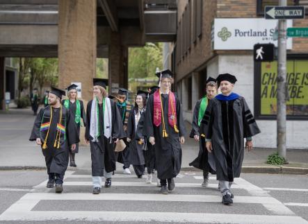 PSU graduates in caps and gowns cross a downtown Portland street near campus before commencement