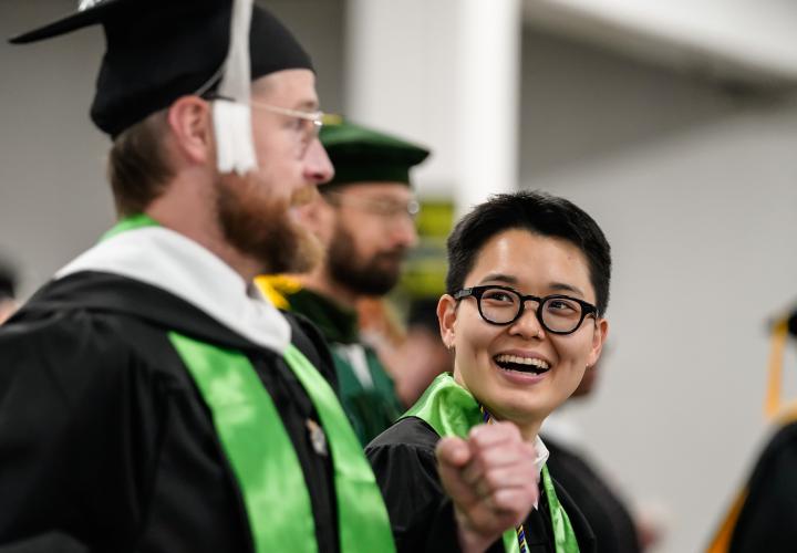 Three graduates in regalia talk amongst themselves