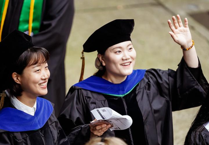 Two graduates in regalia wave to crowd