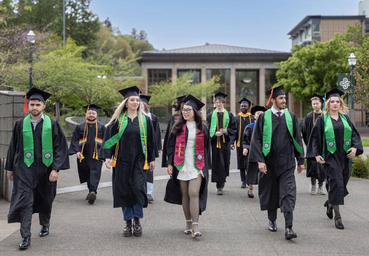 Graduates in caps and gowns walk on campus