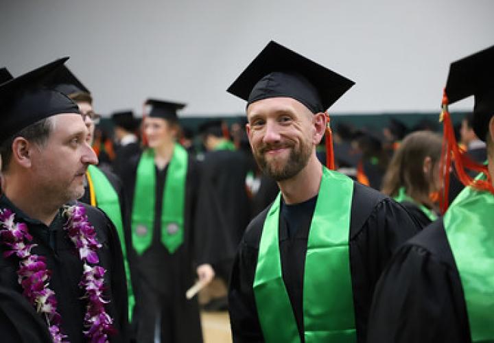 A Maseeh College graduate smiles at the camera in a crowded prep area