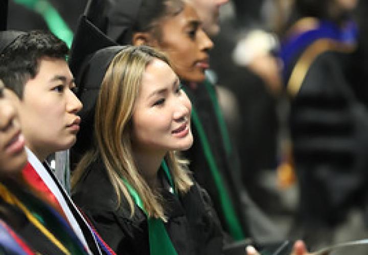 Business graduates seated during the ceremony, wearing regalia and looking toward the stage