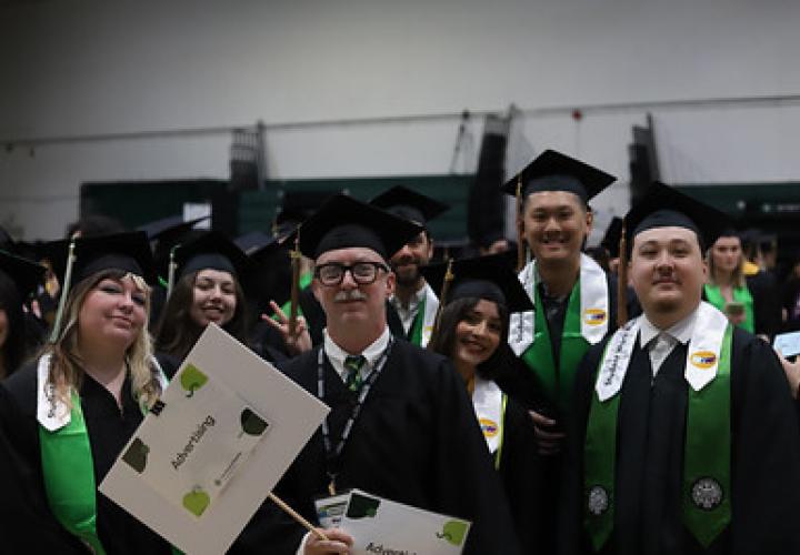 Advertising graduates holding program signs and smiling before the ceremony