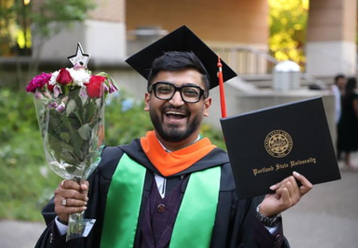Maseeh College graduate holds a diploma cover and bouquet after commencement