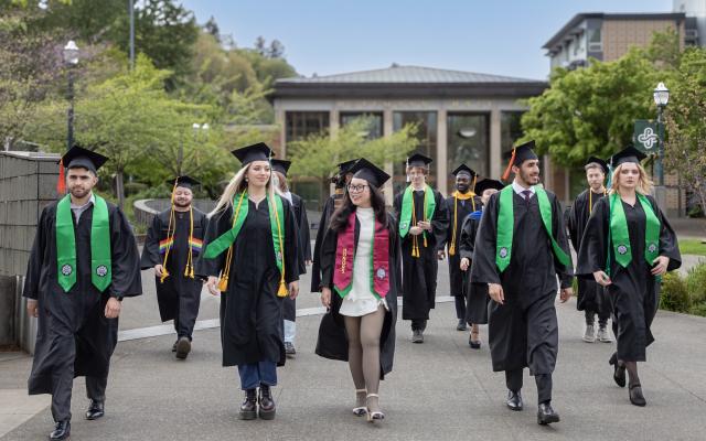 Graduates in caps and gowns walk on campus