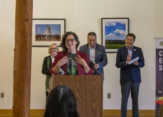 A woman in a purple blazer is happily speaking to a crowd. 