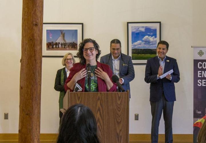 A woman in a purple blazer is happily speaking to a crowd. 