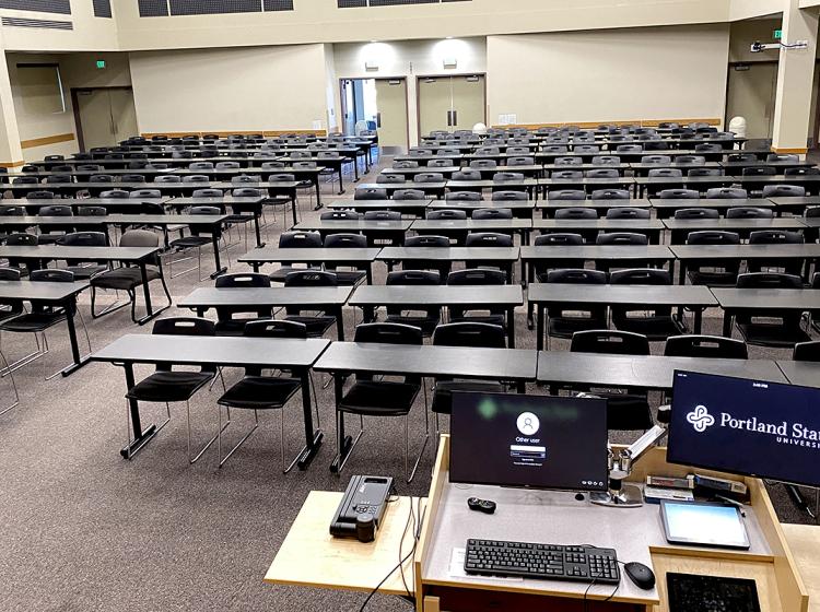 Interior of Hoffmann Hall with classroom chairs and tables filling the floor area. In the back of the room a set of doors leads out of the hall.