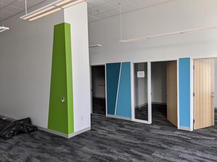 A freshly painted white wall with a long, green rectangle painted on the corner in front of a wall with several doors and blue painted shapes between each office door