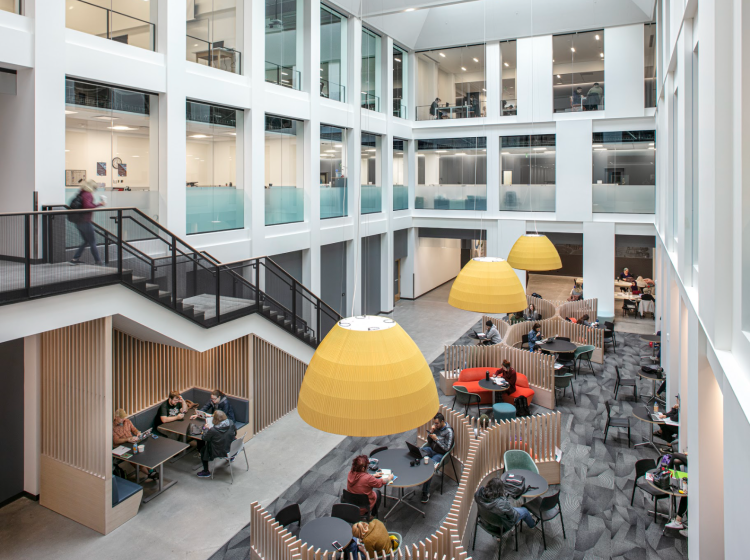 Overlooking the central portion of the inside of the building, a staircase leads down to the main floor that is surrounded by windows looking into classrooms; students gather in the study spaces created on the main floor 