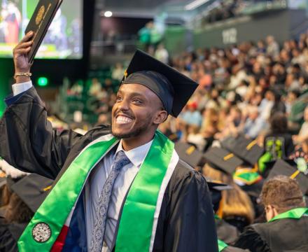 student wearing a cap a gown and holding up a diploma