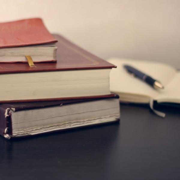 Stack of books and notepad with pen on a desk