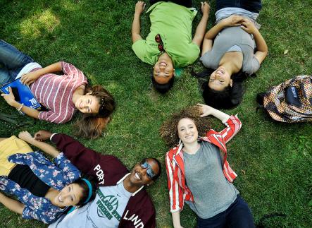 Students lying in grass looking up at camera