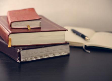 Stack of books and notepad with pen on a desk