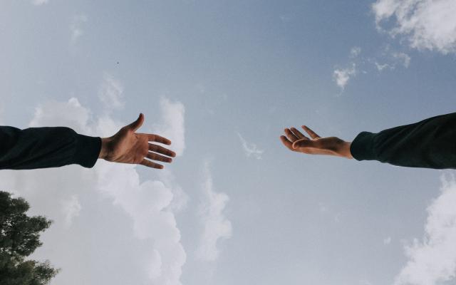 Hand reaching for another hand with sky in the background