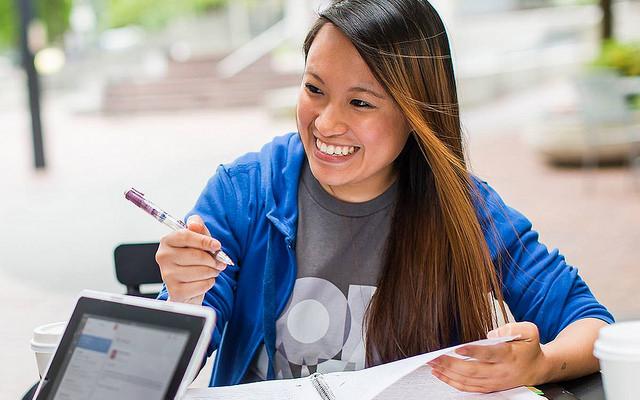 Student smiling outside while writing in a notebook