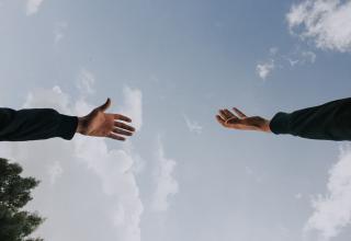 Hand reaching for another hand with sky in the background