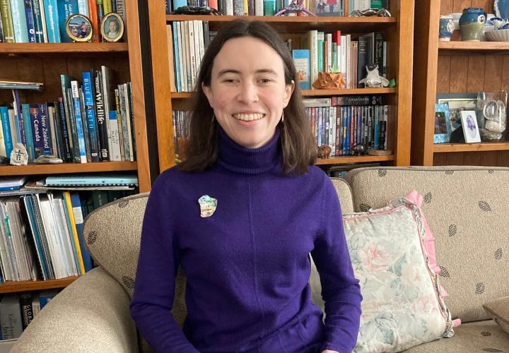 Photo of Aine Kelly-Costello sitting on couch in front of large bookshelf