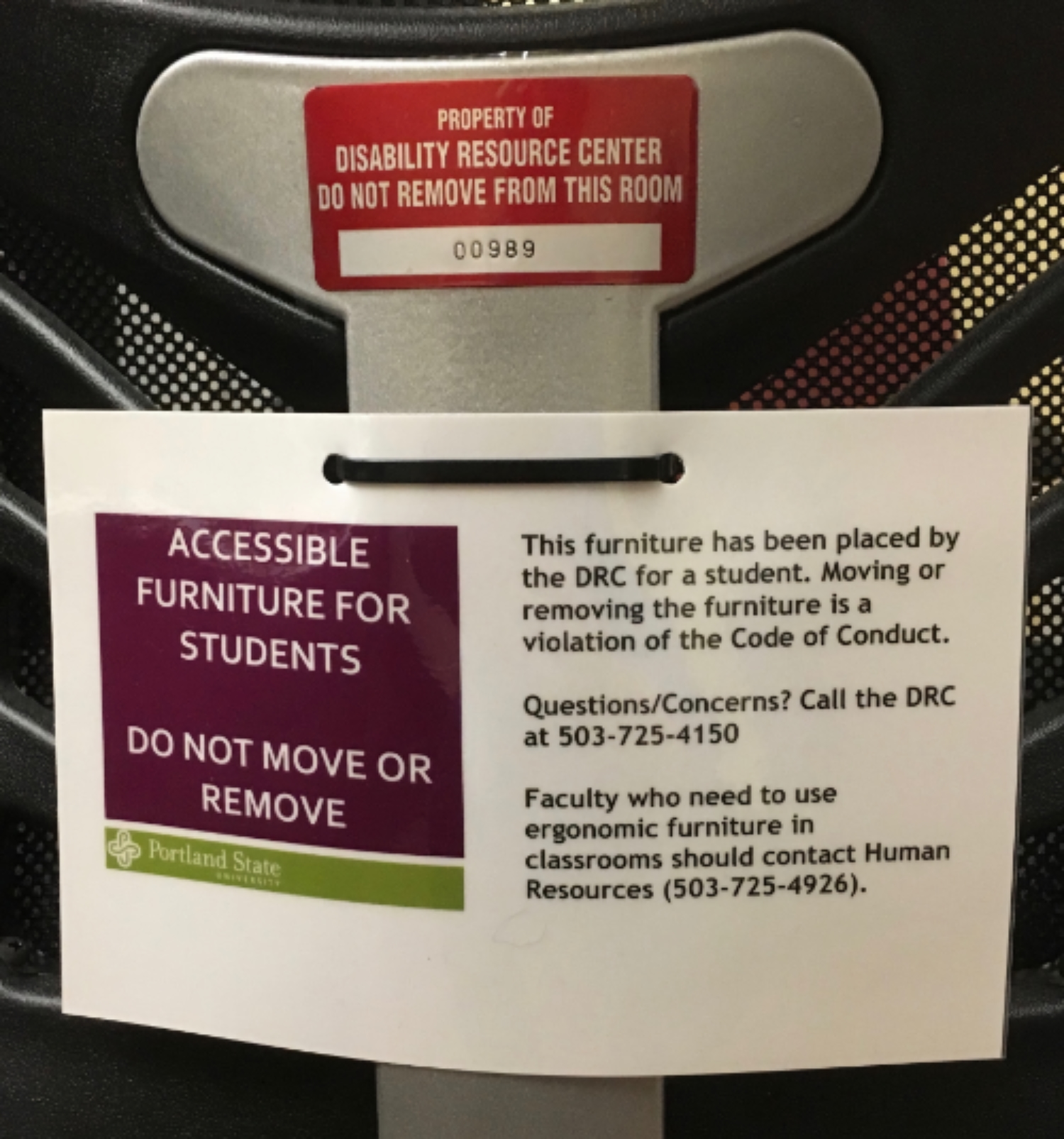 Back of chair with a red label with numbers with text: "Property of Disability Resource Center Do not remove from this room" and white label with purple box with text: "accessible furniture for students do not move or remove".