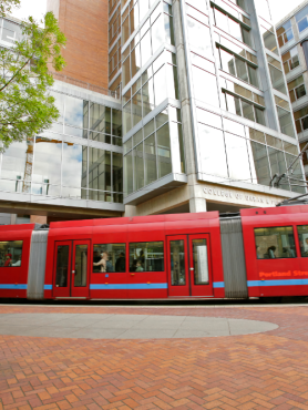Photograph of PSU's urban plaza with bright red trolly in foreground and a tall building in the background