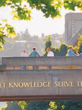 Photograph of skybridge with PSU's motto: "Let Knowledge Serve The City". Five people are standing on the skybridge, talking to each other.