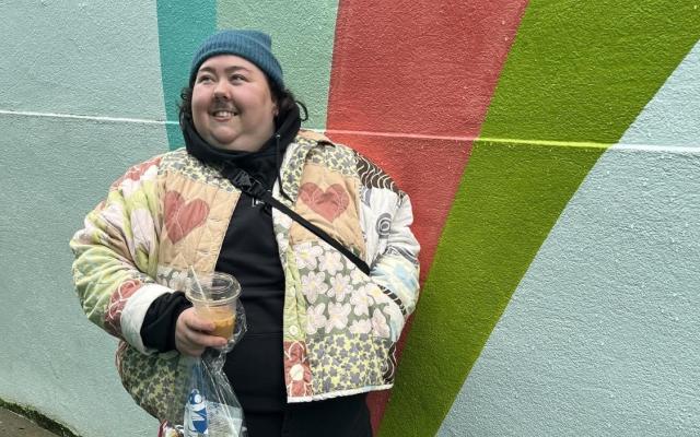Photo of Gracie Sheets, standing outside, smiling and holding a coffee.