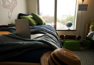 Dorm room with laptop on bed and window in background