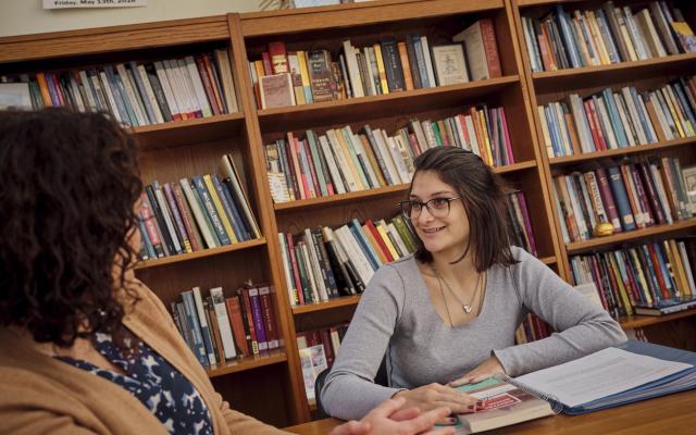 Student with faculty advisor with bookcases in background 