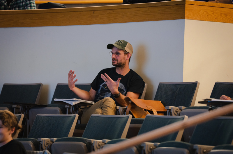 A Portland State student sits in a lecture seat, actively speaking and gesturing with both hands during a seminar.