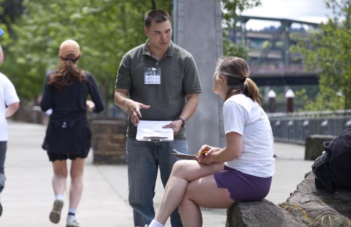 Student surveyer asking passer-by question along waterfront walking path