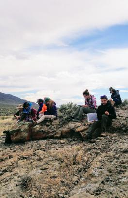 A group of Portland State students taking notes while sitting on rocks during geology fieldwork in a high desert landscape in SE Oregon.