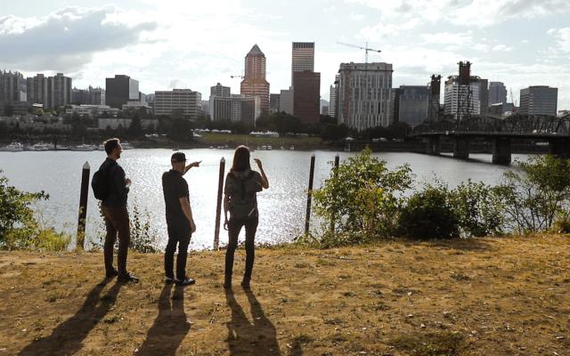 Professor and students at river’s edge pointing to city skyline