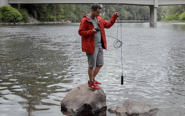 Student standing on rock collecting sample from river