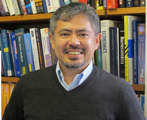 Photo of Hiro Ito from the chest up standing in front of a filled bookcase.