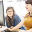 Two female students sitting and looking at a laptop.