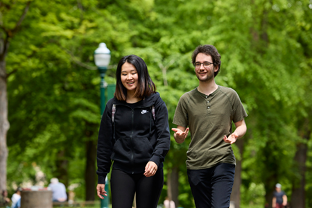 A pair of students walk through the Portland Park Blocks, smiling and talking.