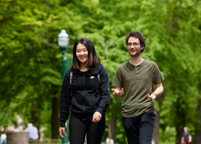A pair of students walk through the Portland Park Blocks, smiling and talking.