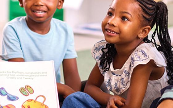 Three young children sit on the floor attentively listening to story time.