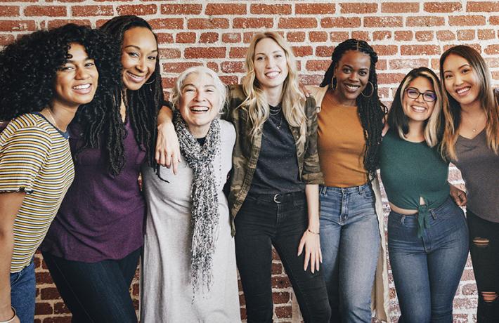 Diverse women beaming with their arms looped around each other