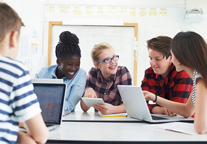 A group of teenagers are gathered together on laptops and tablets.