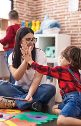 A young woman with long, dark brown hair and glasses high fives a child in a red flannel shirt and denim overalls.