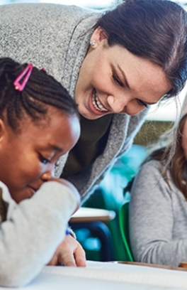 A Caucasian teacher with dark brown hair pulled back assists two students with their classwork.